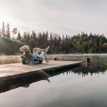 Junge Frau liegt auf einem Steg am See und denkt darüber nach, wie man gute Fenster finden und die passenden Kriterien wählen kann.