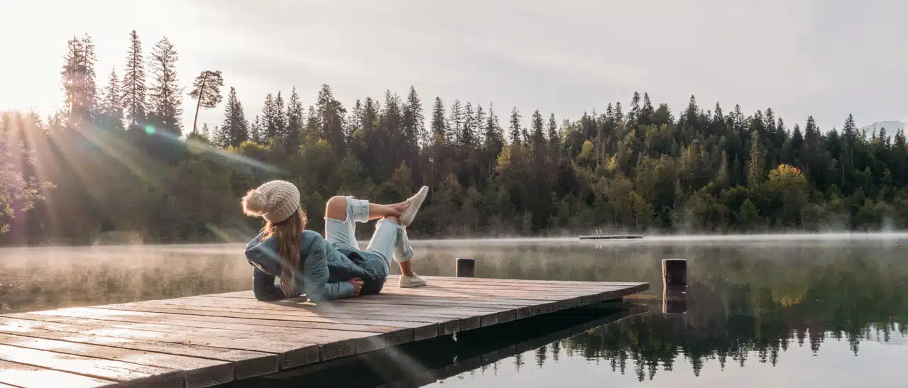 Eine junge Frau sitzt auf einem Steg am See und überlegt, wie sie gute Fenster finden kann.