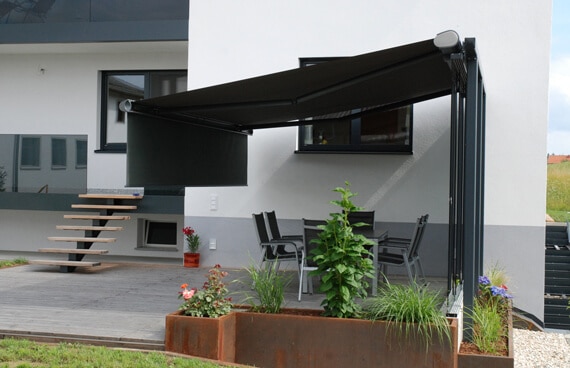 Eine Windschutz Schiebeanlage Terrasse schützt vor Zugluft und bleibt trotzdem offen. Die Glasflügel lassen sich je nach Wetter auf- oder zuschieben, und die Aussicht bleibt erhalten.