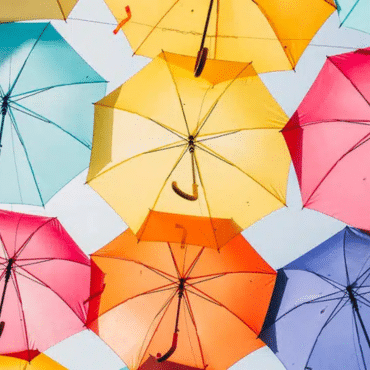 Wintergarten-Beschattung Symbolbild mit vielen bunten Regenschirmen vor hellem Himmel