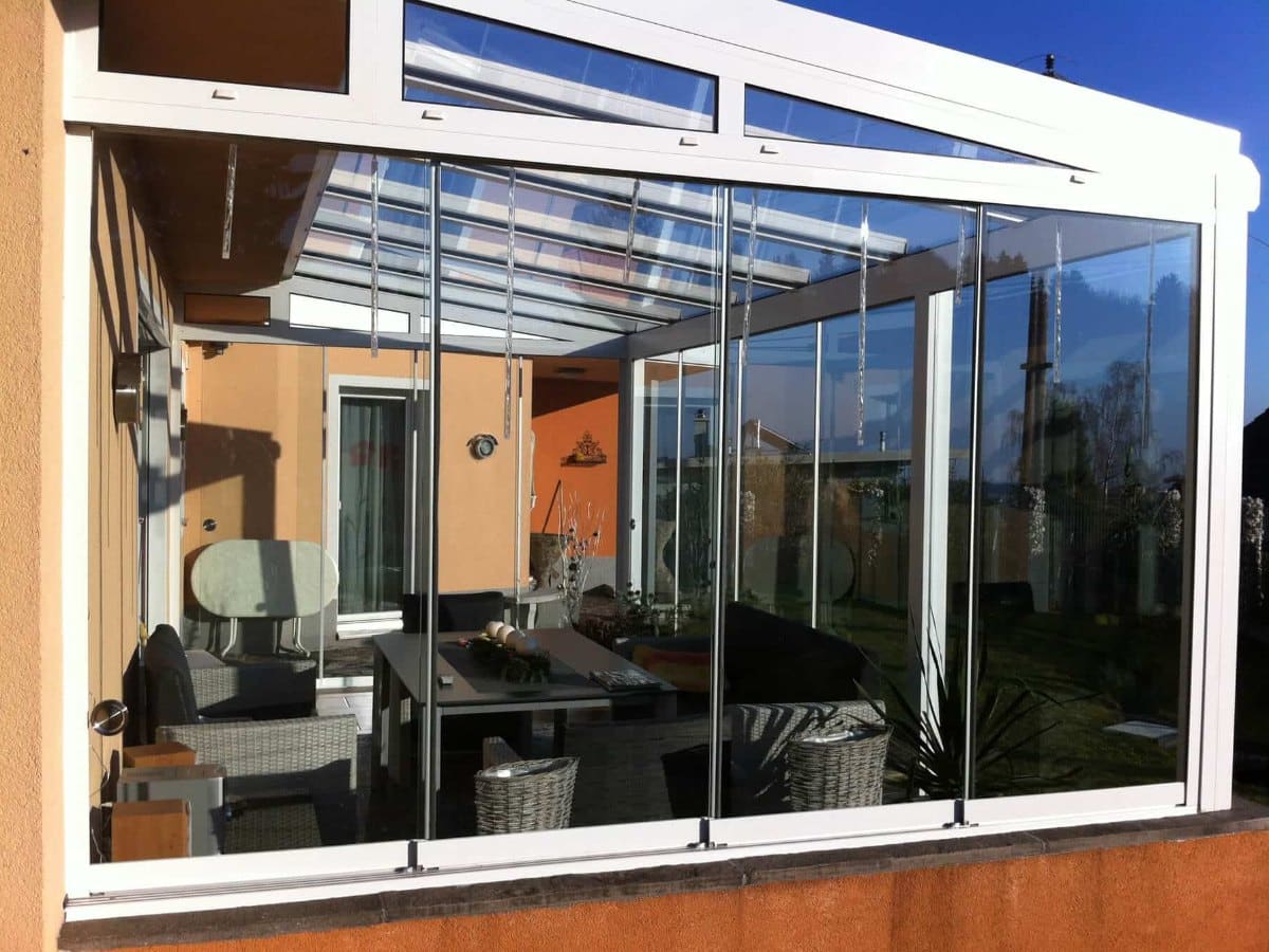 Rahmenlose Glasschiebewand außen vor einem Wintergarten