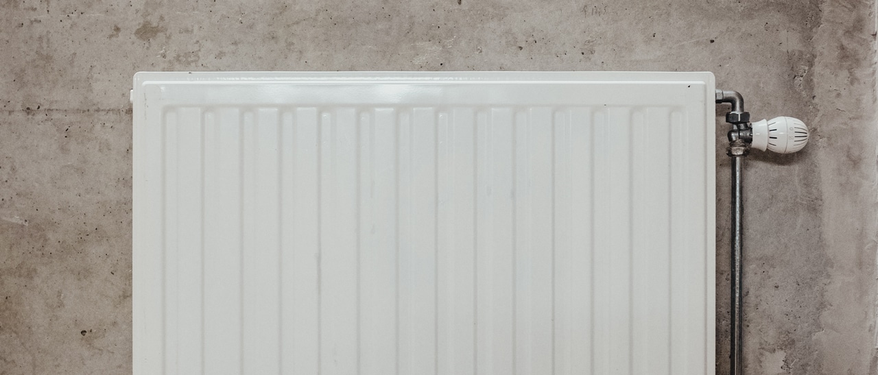 Das Foto zeigt einen schlichten, weißen Heizkörper mit Thermostatventil an einer grauen Betonwand. Solche Heizkörper eignen sich zur dauerhaften Beheizung von Wintergärten und bieten gleichmäßige, regulierbare Wärmeleistung.