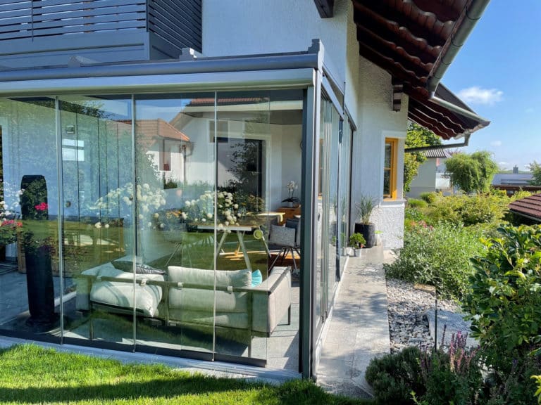 Grauer Wintergarten mit Glasschiebetüren an der Hausecke, Ansicht vom Garten