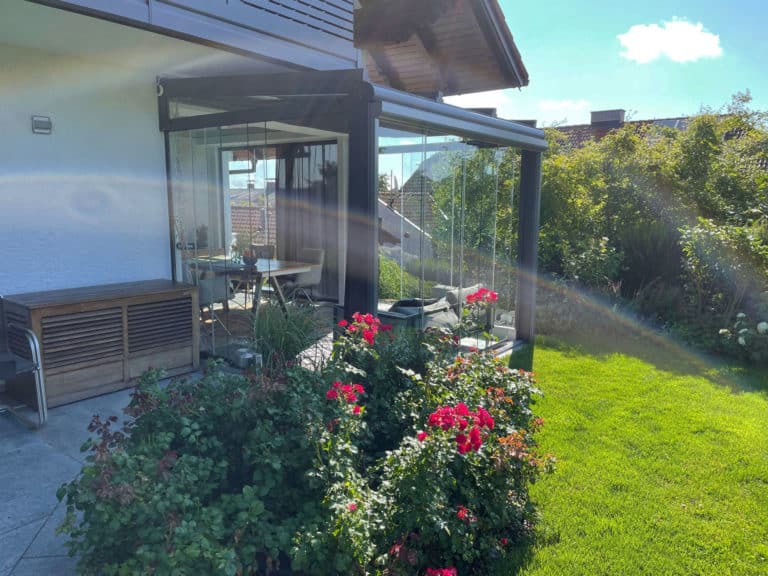 Grauer Wintergarten mit Glaswänden hinter dem Rosenbeet