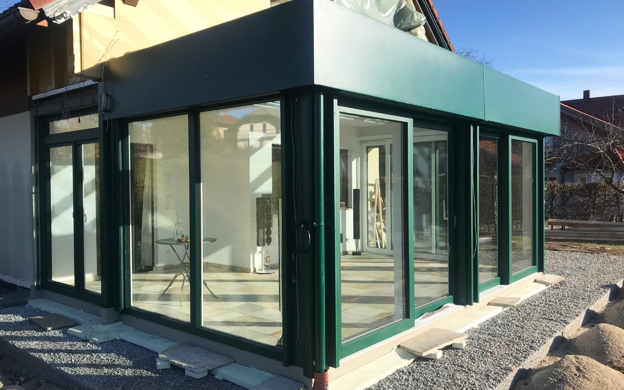 Aluminium-Wintergarten mit Flachdachoptik in Moosgrün und großen Glasflächen an einem Einfamilienhaus am Mondsee im Bezirk Vöcklabruck