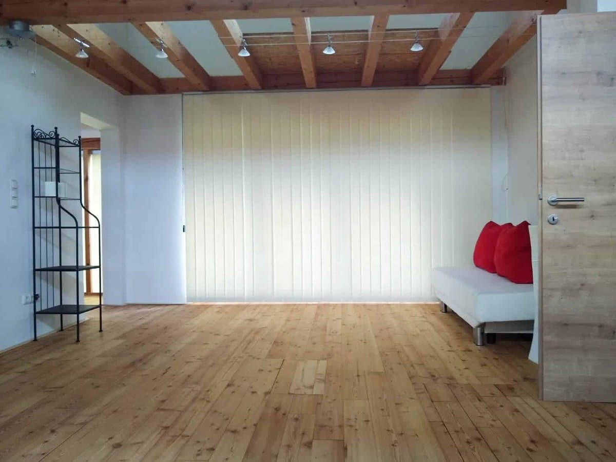Weiße Vertikaljalousien innen vor einer Glas-Faltschiebetür unter einer Holzdecke