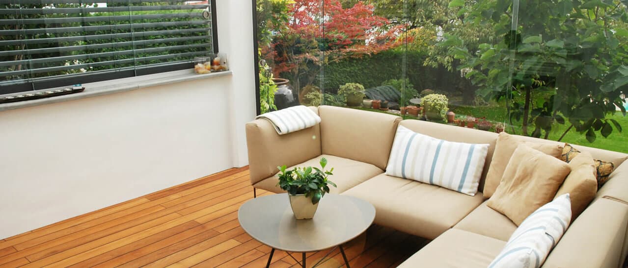 Zu sehen ist ein verglaster Wohnraum mit Sitzmöbeln, Pflanzen und viel Tageslicht, der als Wintergarten genutzt wird. Optimale Planung ist Voraussetzung für Gelingen.