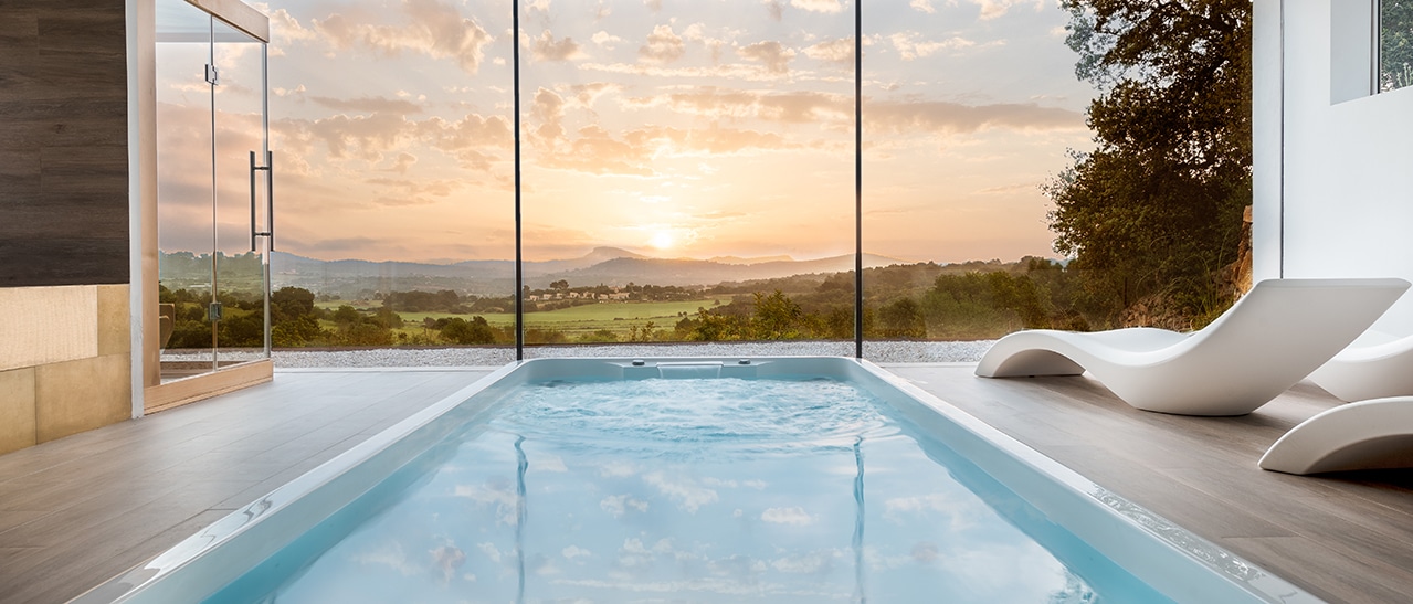 Die Anforderungen an eine Wintergartenüberdachung - moderner Pool mit Glasfront und Aussicht auf Sonnenuntergang über der Landschaft
