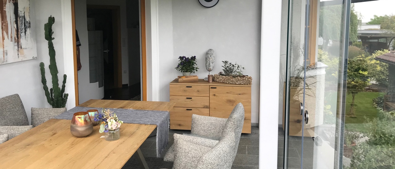 Ein modern-rustikal gestalteter Wintergarten mit Holzmöbeln, warmen Farbtönen und liebevollen Details. Durch Glasflächen und natürliche Materialien entsteht ein wohnlicher Rückzugsort, der Natur und Komfort harmonisch miteinander verbindet.