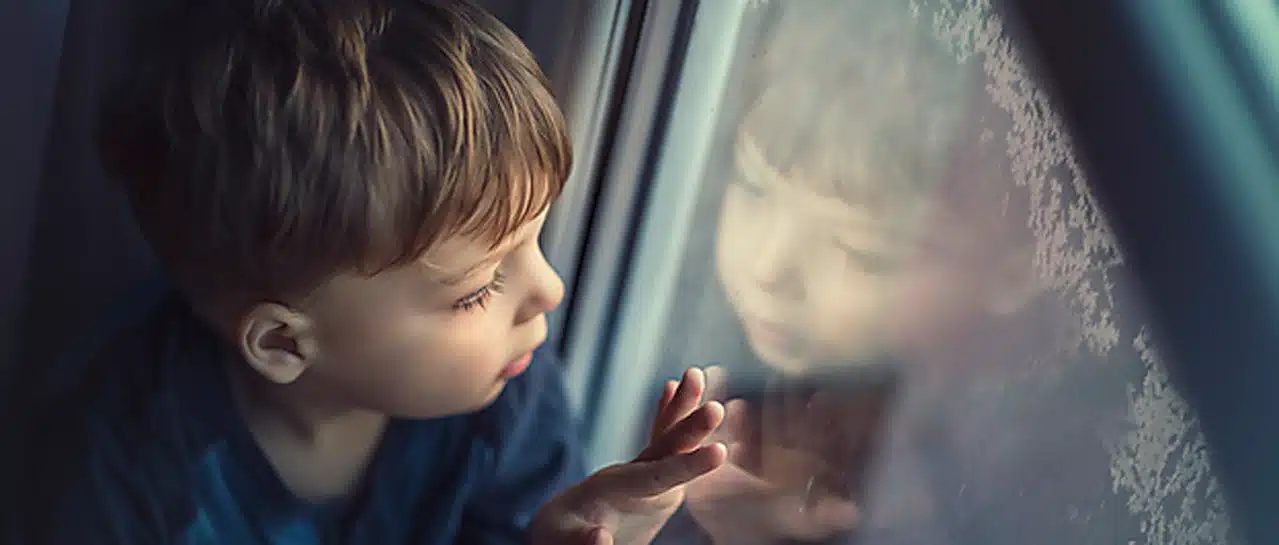 Junge blickt durch Fenster in kalte Winternacht, symbolisiert Gemütlichkeit durch neue Fenster mit Winterrabatt.