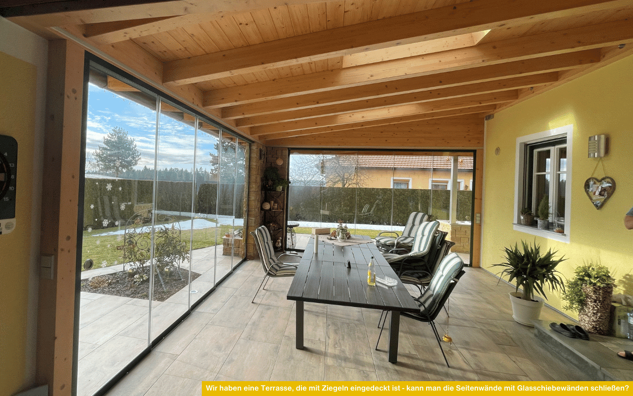 Gemütliche, mit Ziegeln gedeckte Terrasse mit seitlichen Glasschiebetüren für wind- und wettergeschützte Nutzung bei freiem Blick ins Grüne.