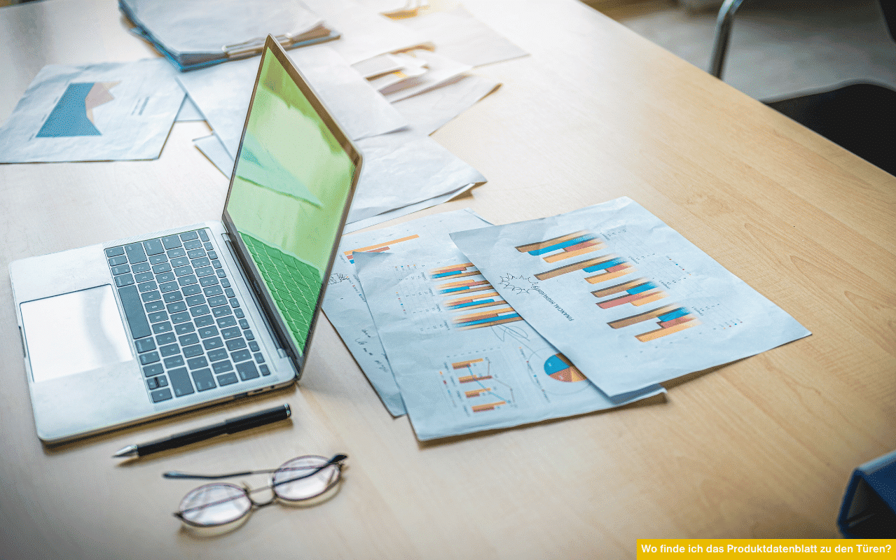 Das Bild zeigt einen Schreibtisch mit einem offenen Laptop, mehreren Diagrammen und Statistiken auf Papier. Eine Brille und ein Stift liegen daneben - es symbolisiert die Analyse von technischen Datenblättern zu Türen.