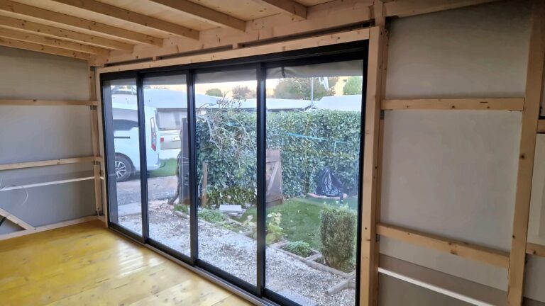 Blick aus dem Wohnwagen-Anbau durch das geschlossene 4-teilige Schiebeelement in den Garten