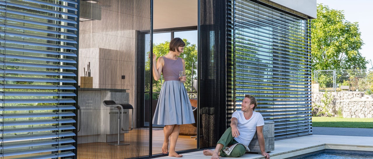 Das Bild zeigt ein modernes Haus mit Fenstern in RAL 7016 Anthrazitgrau. Außenjalousien und ein Insektenschutz-Schiebeelement ergänzen das Zubehör und sorgen für Komfort, Schatten und harmonische Optik.