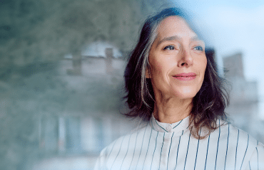 Zufriedene Frau blickt durch moderne Verglasung. Infos zu Fenster Förderung Österreich für Sanierungsprojekte.