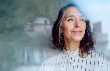 Zufriedene Frau blickt durch moderne Verglasung. Infos zu Fenster Förderung Österreich für Sanierungsprojekte.