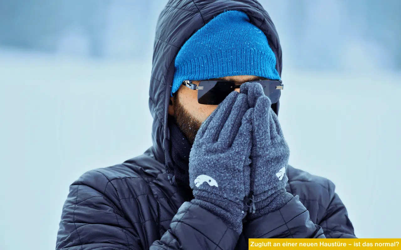 Mann in dicker Winterbekleidung schützt sein Gesicht vor Kälte; symbolisiert Zugluftprobleme bei Haustüren.