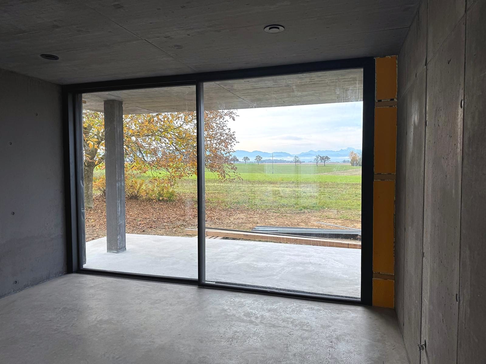 Zweiflügeliges wärmegedämmtes Aluminium-Schiebefenster im Rohbau mit Blick auf Baum, Felder und Alpen, Oberösterreich